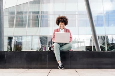 Woman uses a laptop while sitting outside an office building.